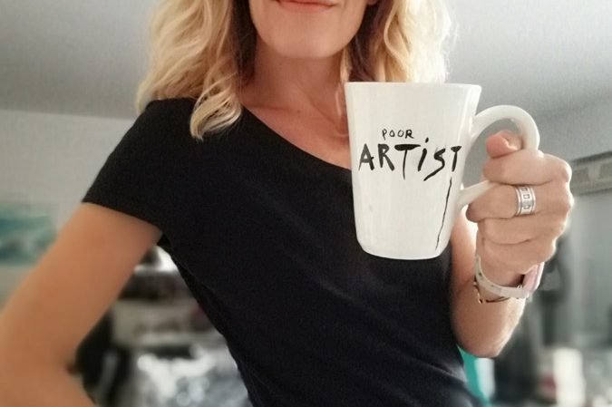 Blonde woman in black sunglasses holding poor artist ceramic mug