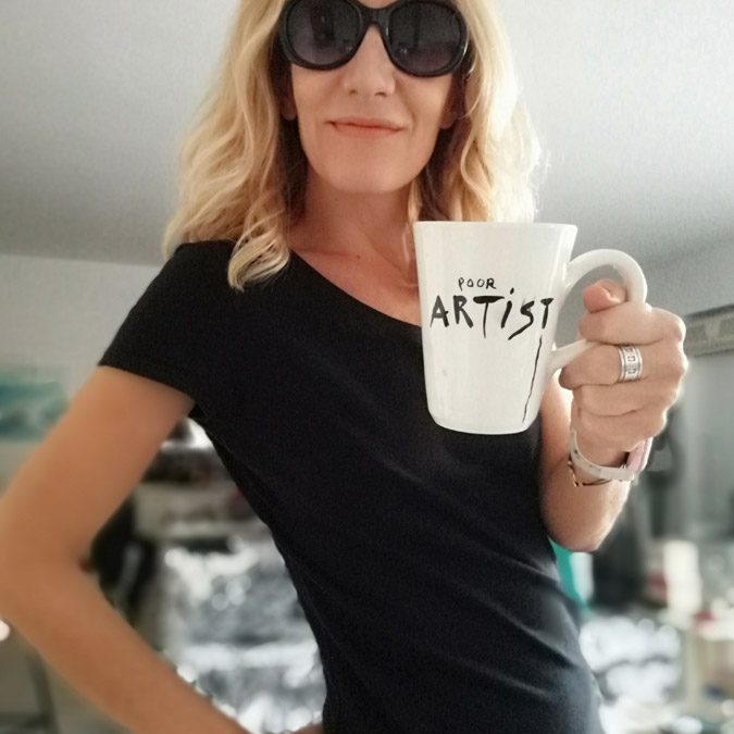 Blonde woman in black sunglasses holding poor artist ceramic mug