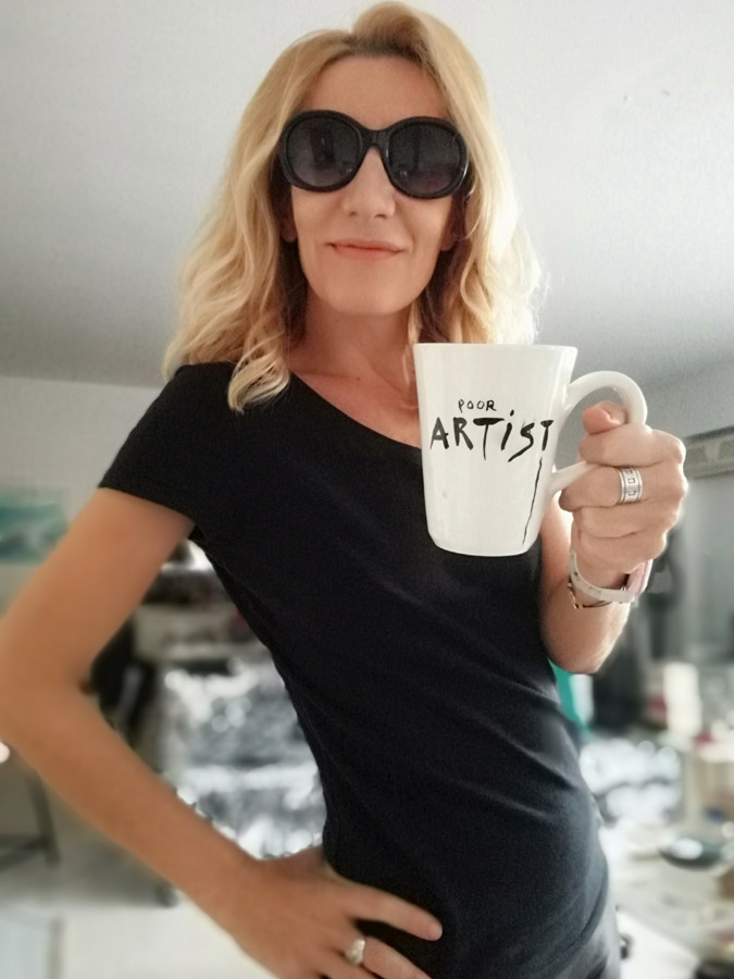 Blonde woman in black sunglasses holding poor artist ceramic mug