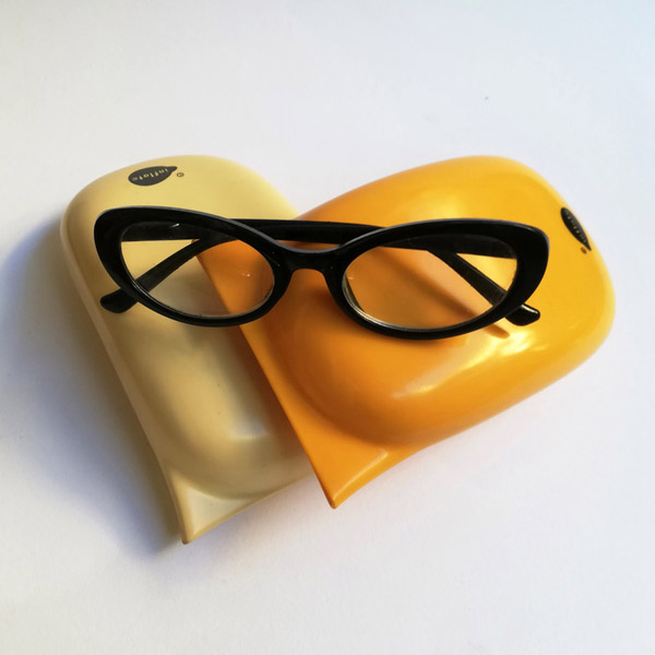 A cream and a yellow dip moulded plastic sunglass case and a pair of black reading glasses.