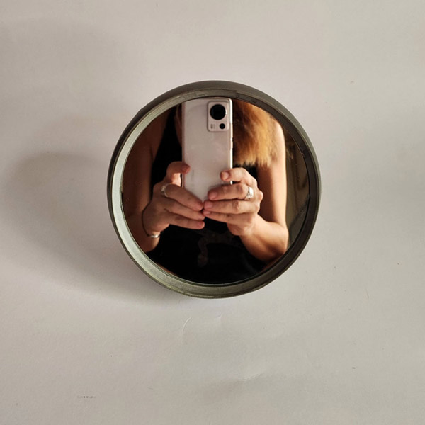 Woman taking a selfie in front of a silver plastic mirror.